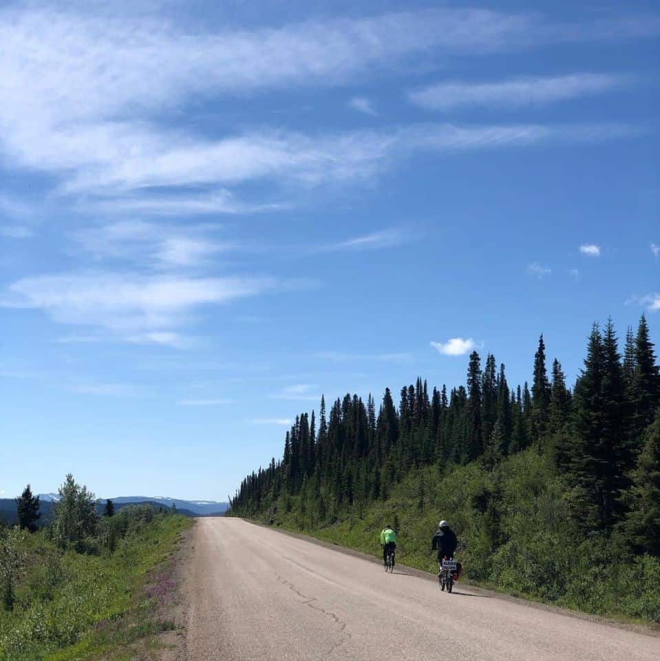 Two cyclists riding on an isolated road in Canada's north on a beautiful day