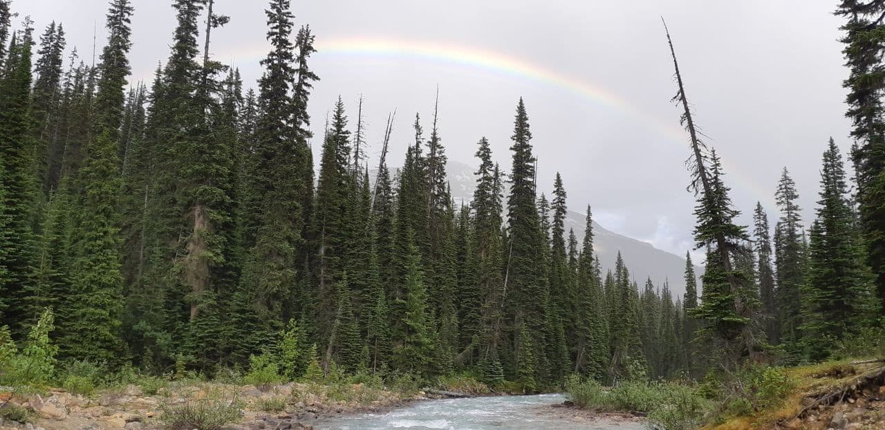A rainbow shines overtop of a mountain peak at Twin Falls Campground in Yoho National Park BC Canada