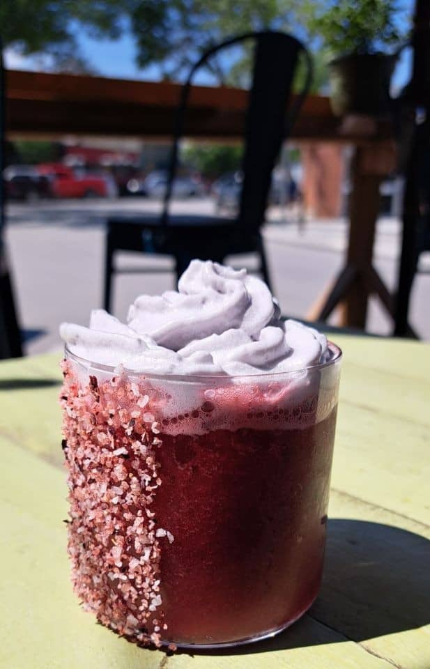 A cocktail made with blackberry puree, lemon, and a hibiscus salt rim topped with a lavender coconut foam at Reposados Tacos in Golden BC Canada