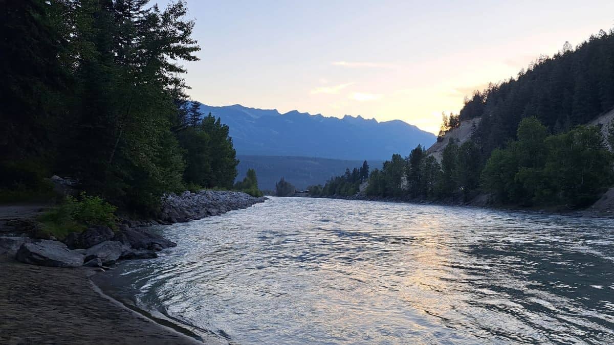 The sunsets behind the mountains casting its golden light on the Kicking Horse River in Golden British Columbia Canada
