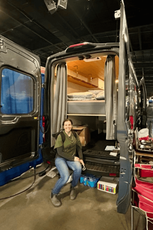 A woman sits on the rear bumper of a rental Campervan in the International Centre, Toronto during the Outdoor Adventure Show
