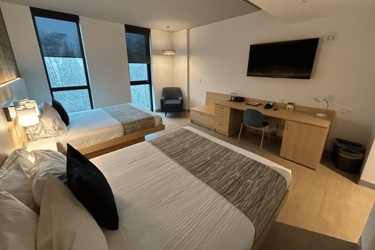 A double queen hotel suite with two beds, corner chair, large television over a desk at Simon Fraser University in Burnaby, British Columbia.