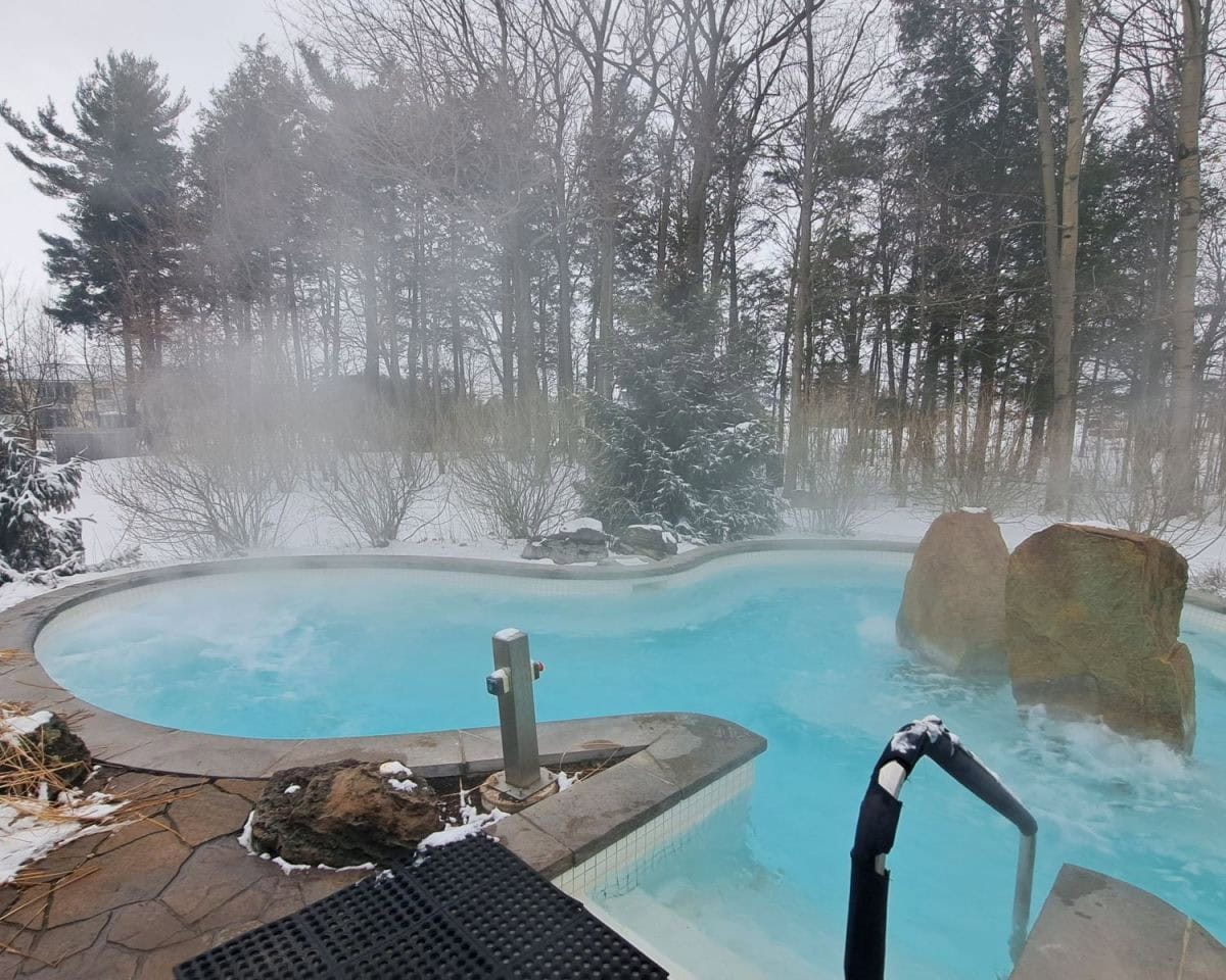Strom Nordic Spa in the Montérégie Region south of Montreal, Quebec, Canada. The image is of a beautiful blue outdoor hot pool surrounded by nature on the edge of Mont Saint Hillaire.