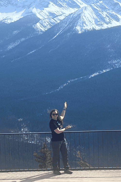 A woman stands at a rail with many snow-covered Rocky Mountain peaks behind her, Banff, Alberta.