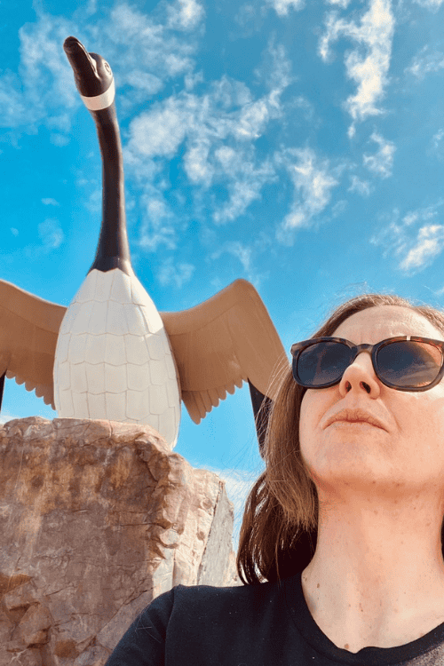 A woman poses with the Wawa Goose, Wawa, Ontario, blue sky, white clouds.