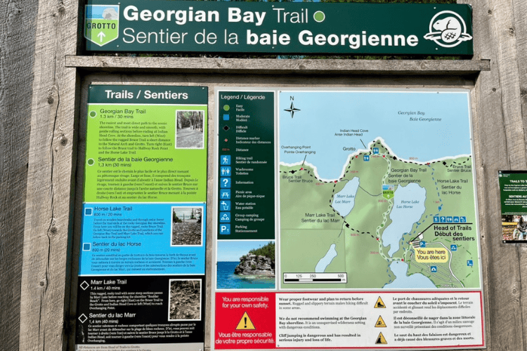 A green and wooden Georgian Bay Trail sign with maps and cautions relevant to the area.