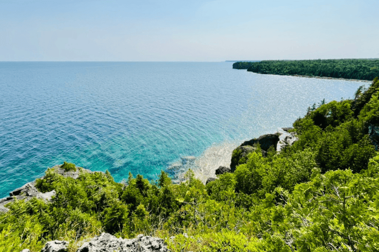 View of lush green forests of the Bruce Peninsula, aqua-blue, crystal clear waters of Georgian Bay, overlooking toward the Grotto from Overhanding Point on the Bruce Trail, Ontario.