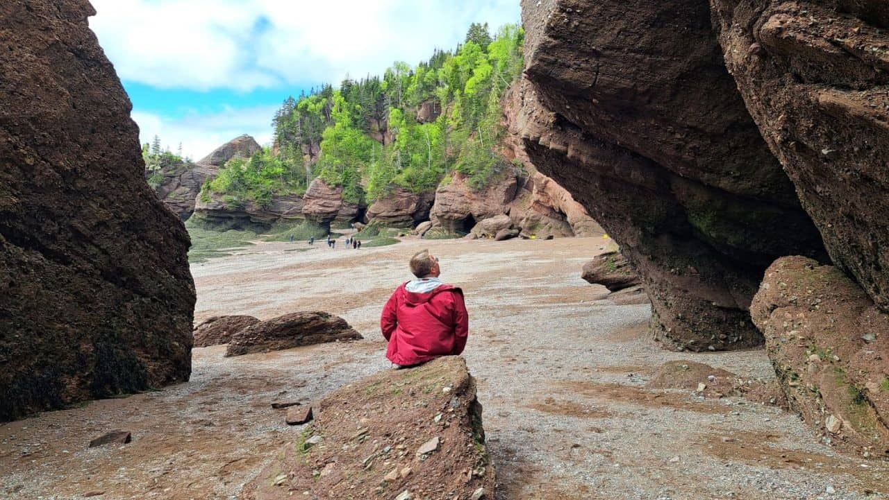 A man sits on a rock on the ocean floor while looking at the massive rock formations at Hopewell Rocks Provincial Park in the Bay of Fundy during low tide in New Brunswick.