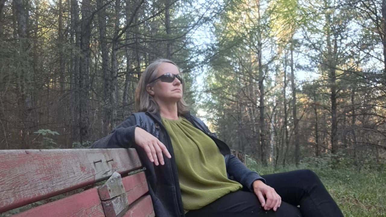 A lady sits on a bench enjoying being in a forest on a warm sunny day