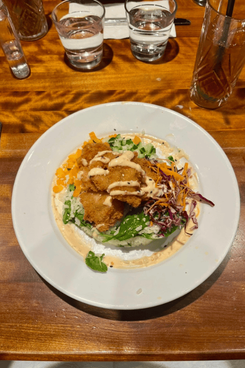 Bang Bang Shrimp as served at La Cage, Bell Centre, Montreal, Quebec. A white dish filled with food sits atop a wooden table.