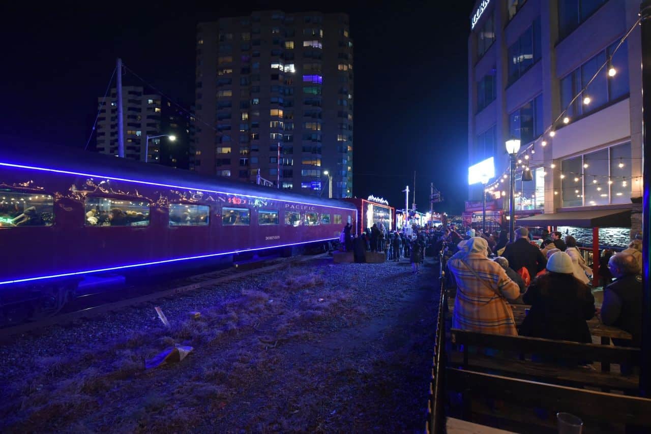 Gathering on the spacious outdoor patio at Molly Bloom's Irish Pub, locals enjoy a prime view of the CPKC Holiday Train in London, Ontario, celebrating the CPKC Holiday Train Crosses Canada tradition.