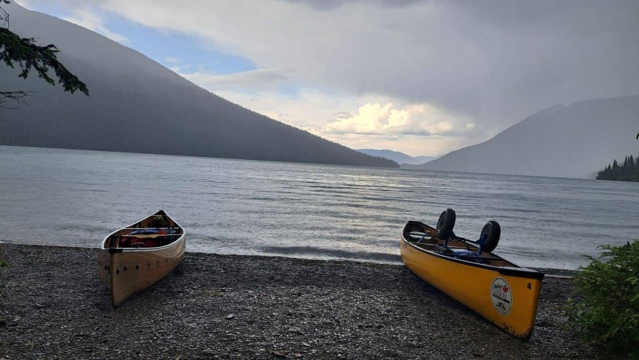 Two canoes are pulled up on the shore of Isaac Lake in Bowron Lakes BC while a thundershower passes by