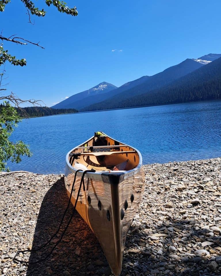 A yellow canoe is pulled up on a rocky beach at the Moxely Creek campround (#18) pointing out across Isaac Lake on the Bowron Lake Canoe Circuit in BC