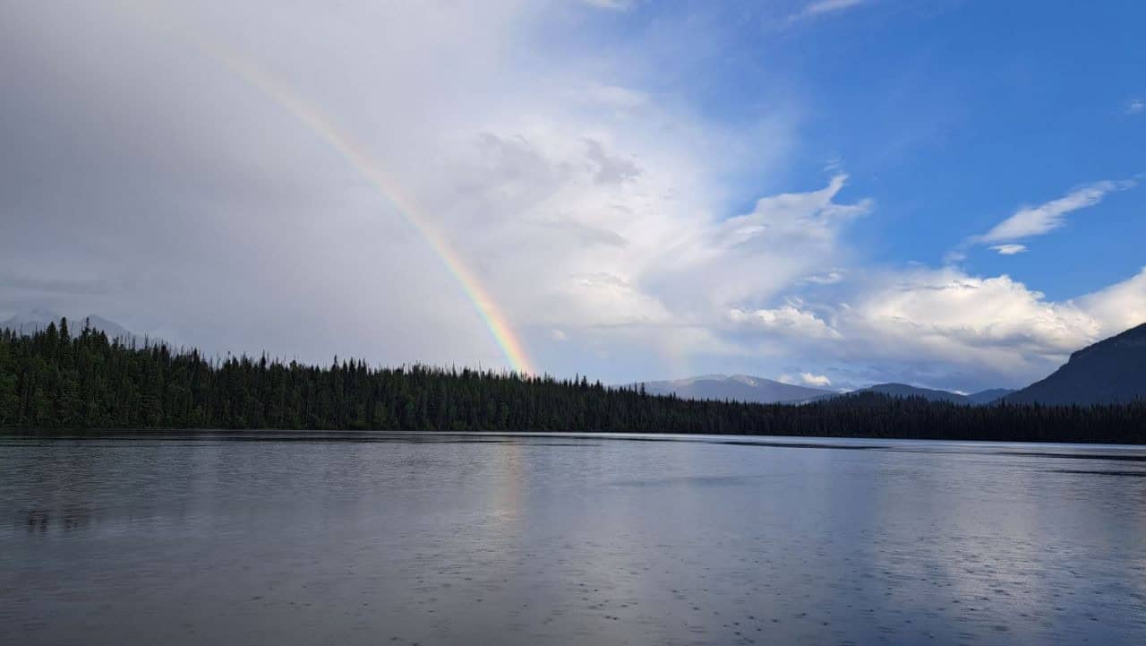 A rainbow separates the blue sky and sunshine from the passing storm clouds over Unna Lake on the Bowron Lakes Canoe Circuit.