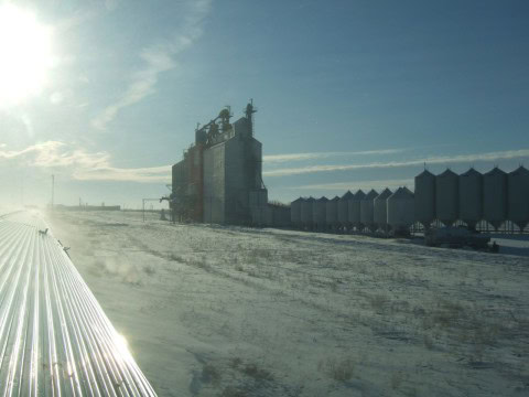 Rows of frost-covered grain silos rise from the snowy Prairies, iconic landmarks seen from VIA Rail’s The Canadian during a winter journey across Manitoba and Saskatchewan by train.