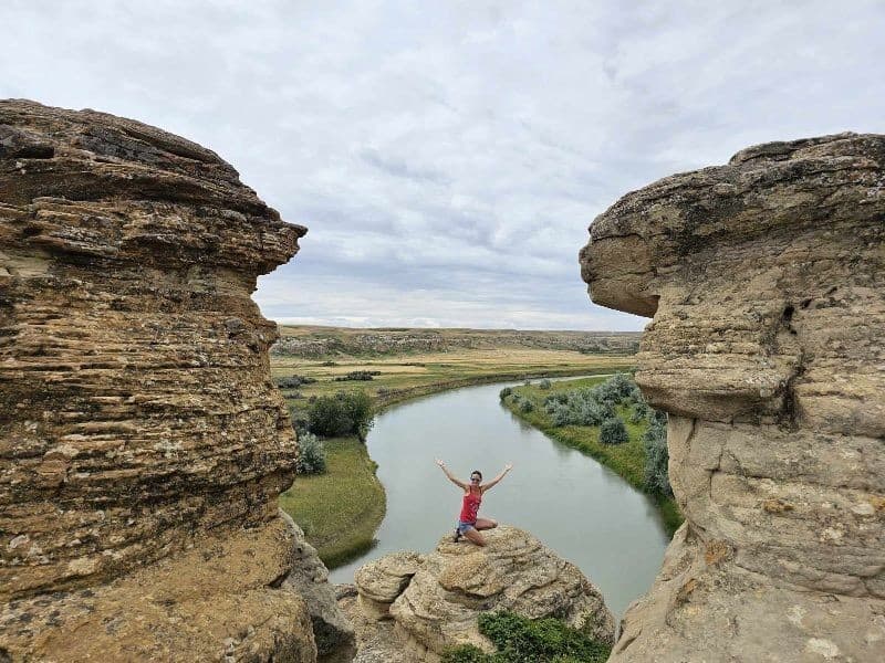 Woman standing between towering rock formations overlooking the Milk River at Writing-on-Stone Provincial Park in Alberta.