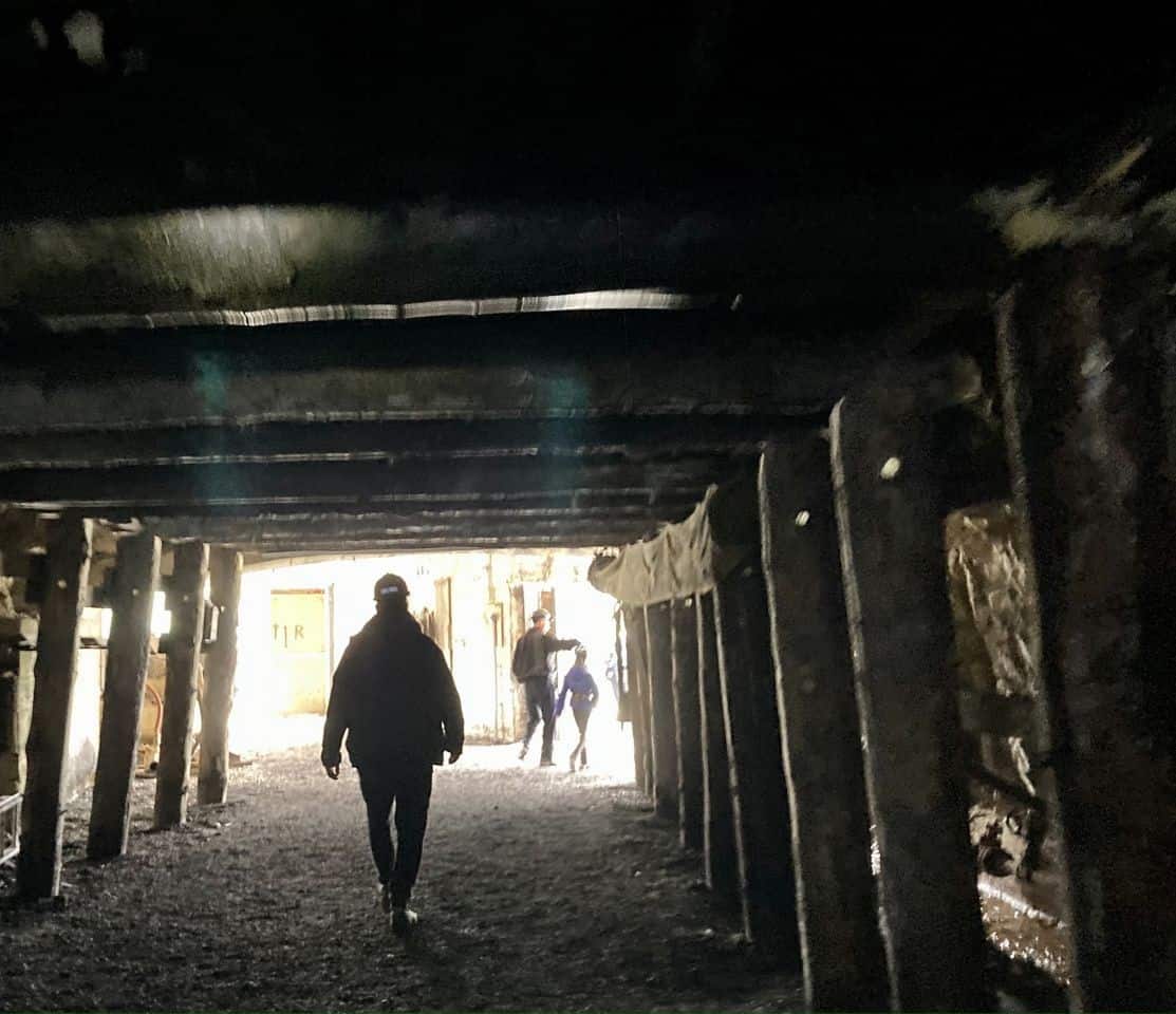 Silouette of two men and a child walking into light from a mine shaft braced with timbers.