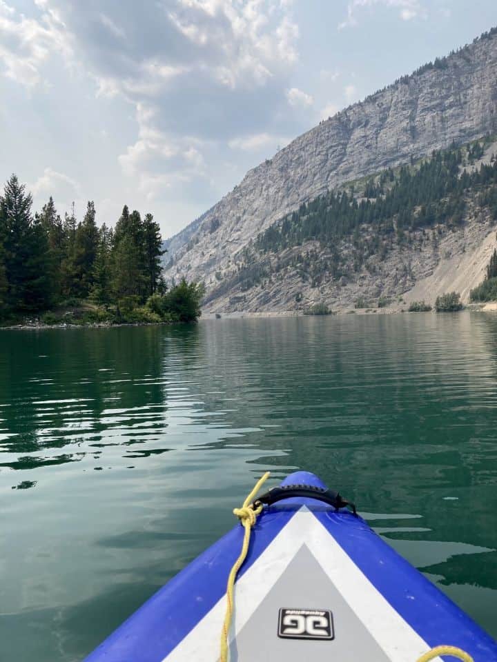 Blue and white inflatable kayak bow on a blue-green lake with mountain in distance.