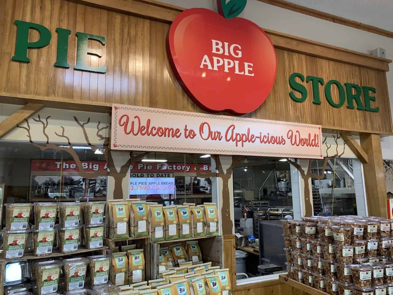 The Big Apple Colborne Ontario Canada 2024-05-20 - In the entrance way, a sign welcomes guests to the Big Apple "apple-icious world!" The large glass windows under the sign showcase the pie and bread making magic in action. 