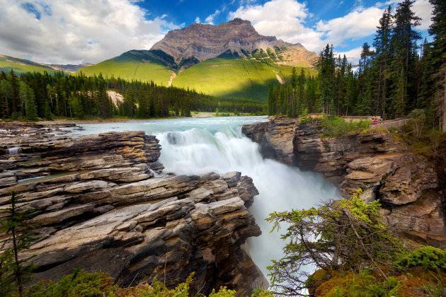 580456195 - Long exposure of powerful Athabasca falls with towering sunlit mountain in background, a short walk from the Icefields parkway between lake Louise and Jasper, Alberta, in summer.